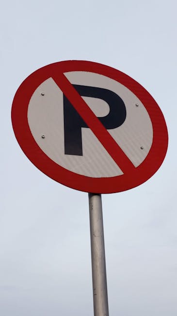 A circular traffic sign featuring a black letter 'P' crossed out with a red diagonal line, indicating no parking. The sign is mounted on a silver metal pole against an overcast sky. The image relates to parking restrictions in Addiscombe, important for home relocation and furniture transport logistics, and reflects considerations for loading areas and parking rules that [COMPANY_NAME], such as Man with Van Addiscombe, must navigate when planning moves or delivery schedules in the area.